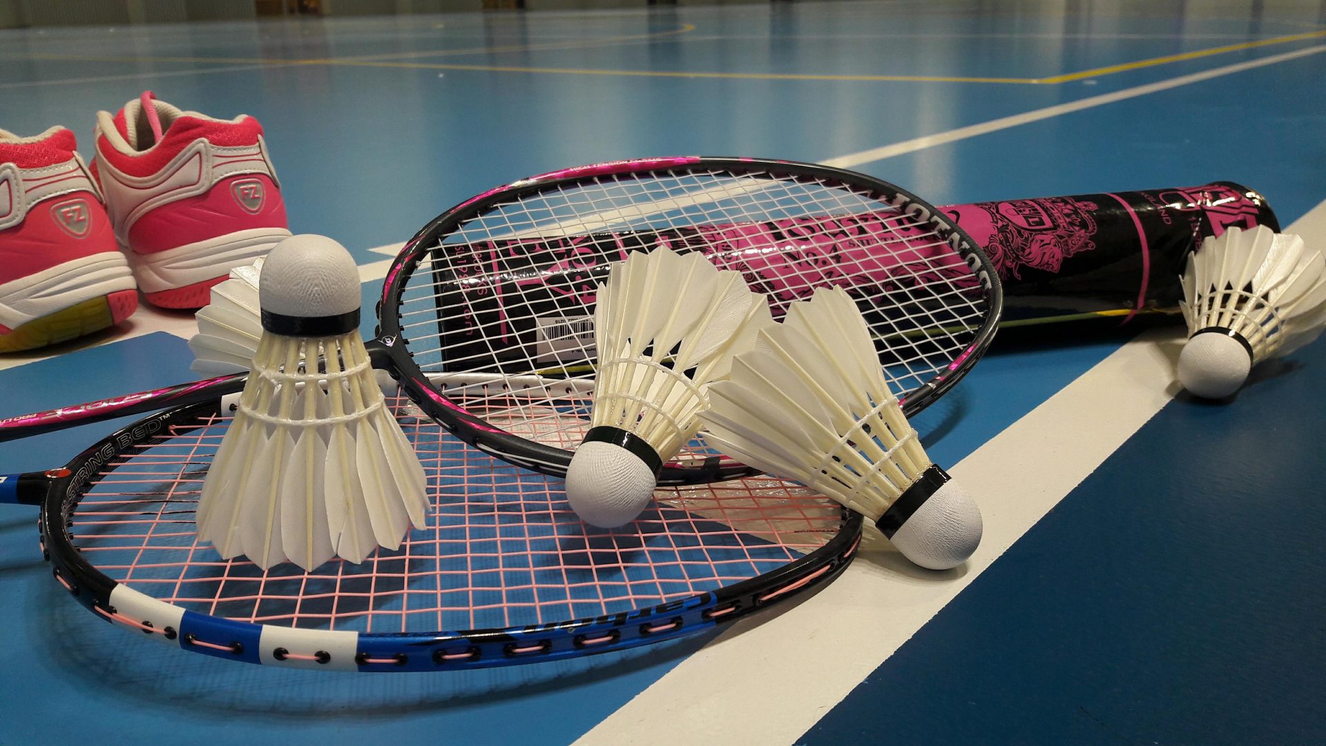 Une paire de tennis rose, deux raquettes de badminton et quatre volants posées au sol