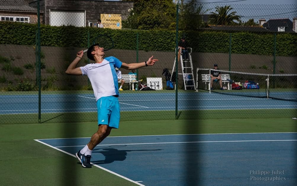 Homme faisant un service smashé, en arrière plan un second court de tennis